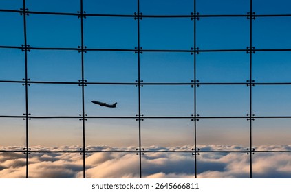 Silhouette of an airplane against a window with square grids and a sunset n the background and clouds below.. The effect looks like the shot was taken from an airplane 