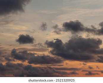 A silhouette of an airplane flying amidst dark clouds during a dramatic sunset. The sky glows with warm tones of orange and gray, creating a moody atmosphere - Powered by Shutterstock