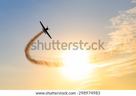 Silhouette of an airplane performing acrobatic flight at sundown. Trace of Smoke behind it