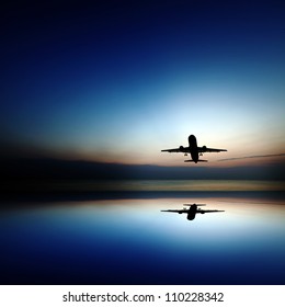 Silhouette of an airplane taking off into a surreal colorful evening sky with reflection.