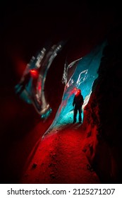 Silhouette Of Alpinist In Helmet With Red Glow Headlamp In Deep Narrow Glacial Ice Cave With Cyan Lights Explore Winter Mountain Glacier In Kazakhstan