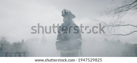 Silhouette of American female firefighter in traditional helmet and full gear standing in the smoke. Shot with 2x anamorphic lens