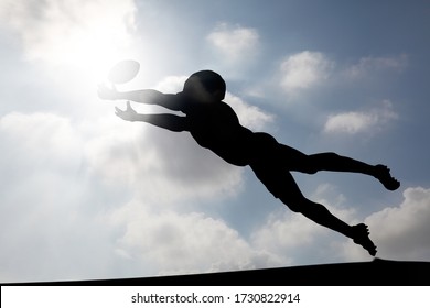 Silhouette Of An American Football Player Diving To Catch A Ball At A Touchdown Zone Against A Cloudy Blue Sky For The Concept: Aim For Glory.