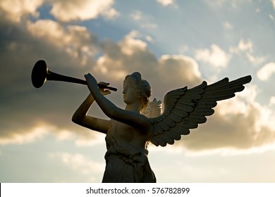 silhouette of angel blowing golden horn during sunrise against dramatic sky 