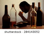 silhouette of anonymous alcoholic person drinking behind bottles of alcohol 