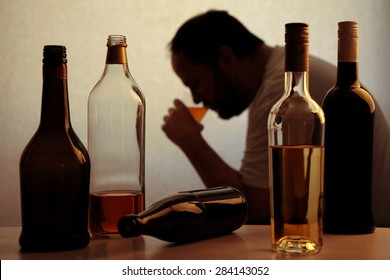 silhouette of anonymous alcoholic person drinking behind bottles of alcohol 