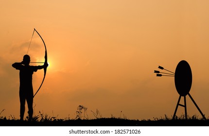 Silhouette archery shoots a bow at the target in sunset sky and cloud.