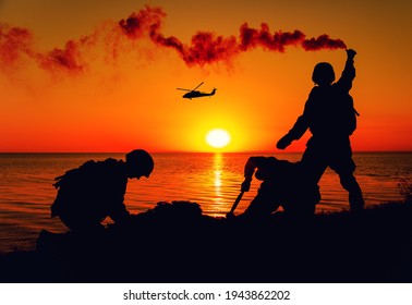 Silhouette of army special forces infantry soldiers, Marines or Navy SEALS team signaling to helicopter with smoke flair while waiting for evacuation, landing on seashore during amphibious operation