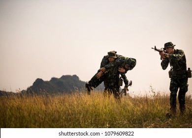 Silhouette Of Asian Army Soldier Carries A Wounded Soldier Evacuate At Across The Deep Forest.