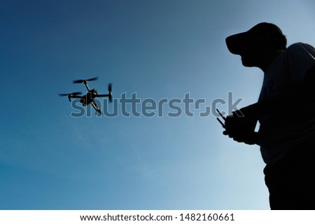 A silhouette of an asian man holds a remote control to control the manoeuvre of his drone.