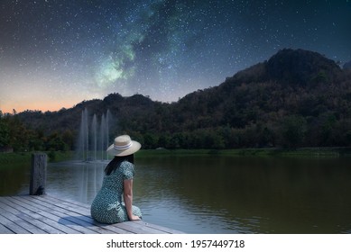 

Silhouette of asian women Sitting by the lake alone Miss your lover and imagine the night atmosphere with the stars and the Milky Way happily. Long exposure, with grain.