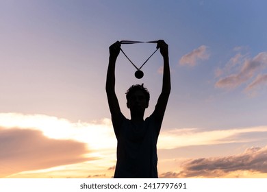 Silhouette of an athlete celebrating the gold medal against a sunset sky adorned with golden clouds in the background. Ideal for conveying the spirit of success in sporting events. - Powered by Shutterstock