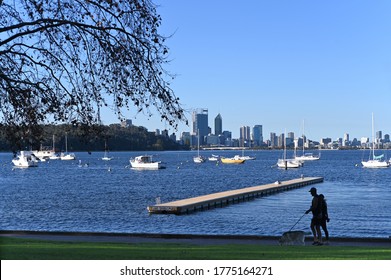 Silhouette Of Australian Couple Walking Their Dog  In Matilda Bay Along The Swan River Against Perth Financial District  Skyline In Western Australia.