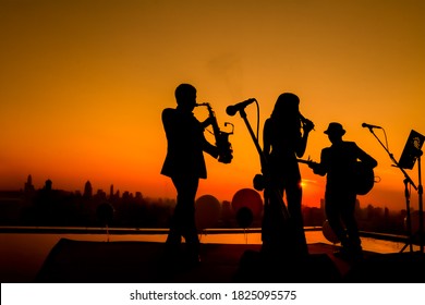 Silhouette autumn or summer scene of 1 woman and 2 men trio musician before twilight time on sky. Trio band showing on sunset light background, Bangkok Thailand