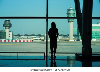 Silhouette Back Portrait Female Traveler Stands Inside The Terminal And Looks Out The Runway And Hanger At The Airport