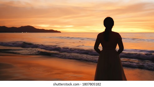 silhouette of back view asian woman standing on the beach during sunset