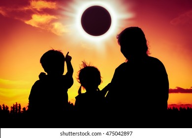 Silhouette back view of family sitting and relaxing together. Boy point to solar eclipse on gold sky background. Happy family spending time together. Outdoor.