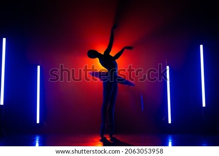 Silhouette of ballerina is practicing elements in studio with neon colorful light. Young woman dancing in classic tutu dress. Gracefulness and tenderness in every movement.