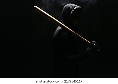 Silhouette Of Bandit In Hoodie Holding Baseball Bat On Black Background With Lighting And Smoke