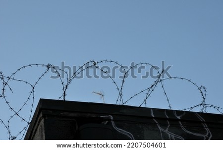 Silhouette of barbed wire on a building against a blue sky