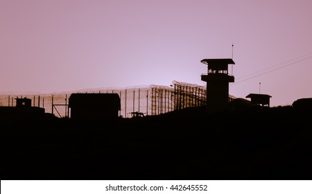 Silhouette of barbed wires and watchtower of prison, at sunset  - Powered by Shutterstock