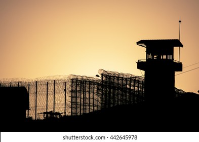 Silhouette de alambres de púas y torre de vigilancia de la prisión, al atardecer 