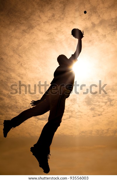 The silhouette of baseball player jumping into air to make the catch
