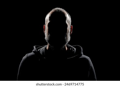 A silhouette of a bearded man wearing a black sweater, in the dark with dramatic lighting to maintain anonymity. - Powered by Shutterstock