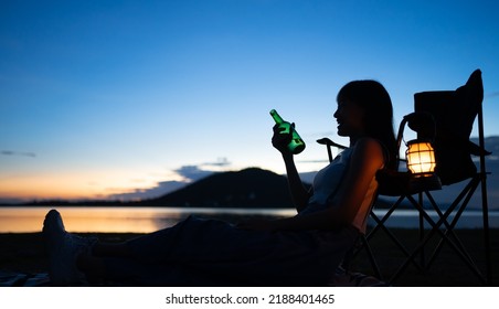 Silhouette Of Beautiful Asian Woman Drinking Beer Out Of A Glass Bottle At Sunset. Beer Bottles And Clanging On The Sunset Beach. Party, Holiday, Summer, Friendship Concept.