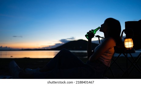 Silhouette Of Beautiful Asian Woman Drinking Beer Out Of A Glass Bottle At Sunset. Beer Bottles And Clanging On The Sunset Beach. Party, Holiday, Summer, Friendship Concept.