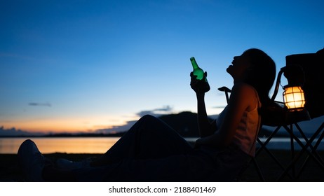 Silhouette Of Beautiful Asian Woman Drinking Beer Out Of A Glass Bottle At Sunset. Beer Bottles And Clanging On The Sunset Beach. Party, Holiday, Summer, Friendship Concept.