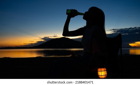 Silhouette Of Beautiful Asian Woman Drinking Beer Out Of A Glass Bottle At Sunset. Beer Bottles And Clanging On The Sunset Beach. Party, Holiday, Summer, Friendship Concept.