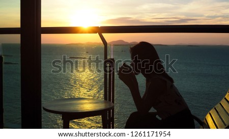 Silhouette of a beautiful Asian woman drinking a cup of coffee with warm afternoon sunset at the ocean in the background.