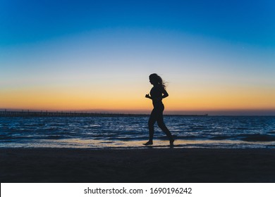 Silhouette of beautiful long hair girl standing on sea beach and looking on sunset. Running and jumping on sea.