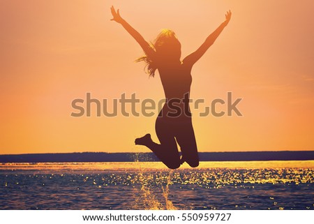 Silhouette of a beautiful, slim girl who jumps on a background of a sunset on the beach.