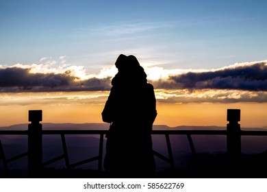 silhouette of a beautiful woman standing on panoramic viewpoint., looking to the horizon and enjoying a beautiful sunset behind the mountain.