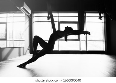 Silhouette of a beautiful young woman doing fly yoga and stretches in the gym.
