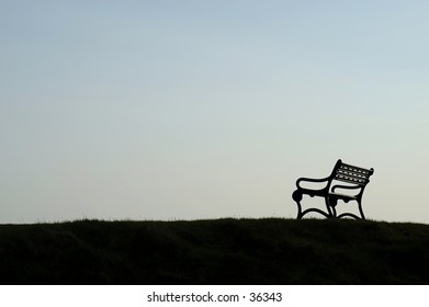 Silhouette Of A Bench On A Grassy Hill.  Lots Of Evening Sky, A Little Bit Of Clouds.  Plenty Of Room For Typeset.