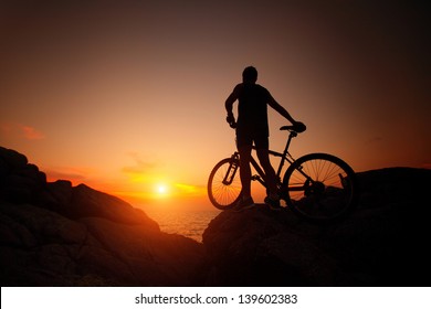 Silhouette Of Bicycle Rider On A Rock At Sunset