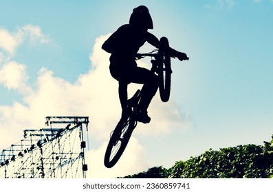 Silhouette of a biker performing an extreme dirty jump with a bmx bike against the sky - Powered by Shutterstock