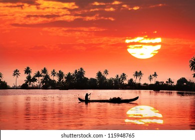 Silhouette of boat and fisherman in backwaters at palms and big orange sun background - Powered by Shutterstock