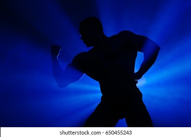 Silhouette Bodybuilder. Silhouette of an athlete in the rays of light. The dark silhouette of a bodybuilder. A man with big muscles.