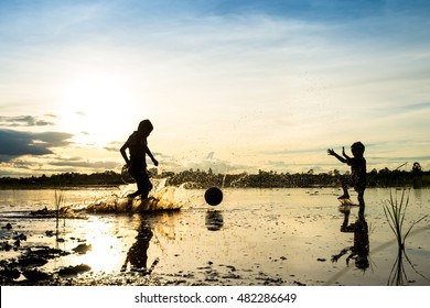 Silhouette of boy playing football in water at countryside in thailand