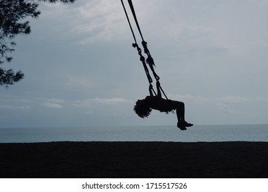Silhouette of a boy swinging on a swing, against the background of the sea