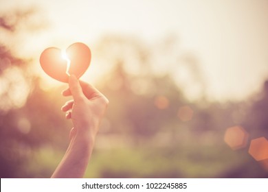 Silhouette broken heart,close up woman hand holding broken heart in the park.
				