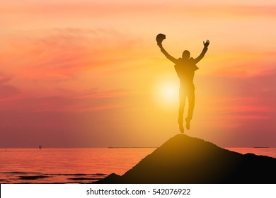 Silhouette Of Business Engineer Man Celebration Success Happiness On A Stone Evening Sky Sunset At Beach Background, Sport And Active Life Concept.