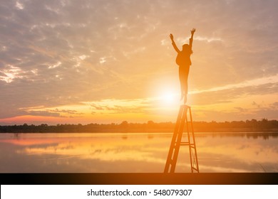 Silhouette of Business woman Celebration Success Happiness on a stairs Evening Sky Sunset at Lake Background, Thinks Big and Dreams Big Concept.