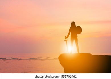 Silhouette Of Business Woman Knight Sword And Shield In Sunset Background, Fighting Business Warrior Concept.