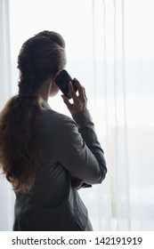 Silhouette of business woman talking cell phone and looking into window