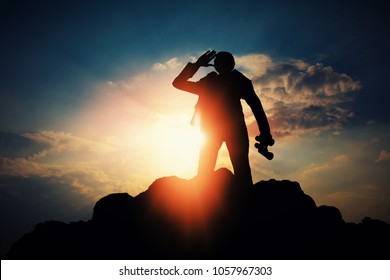 Silhouette Of Businessman With Binocular For Searching A Opportunity On Top Of Mountain Against Sun Light 